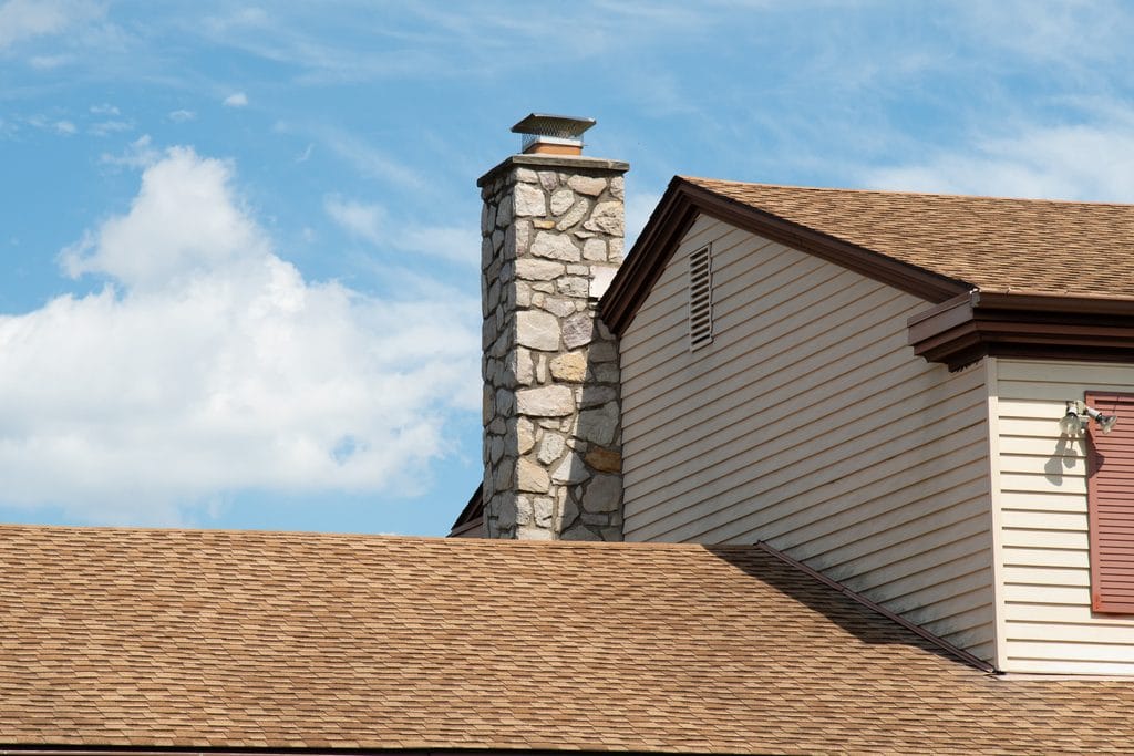 Stone chimney with a cap installed on a residential home with white siding.