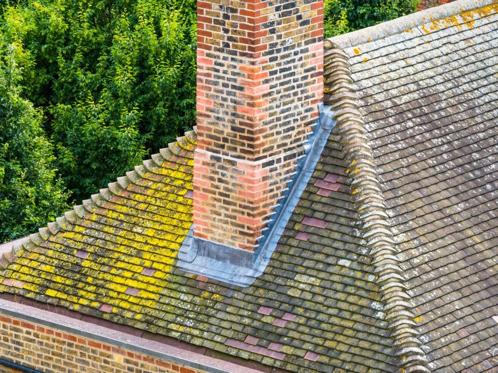 Stepped counter flashing set into the mortar joints of a brick chimney on a tiled roof.