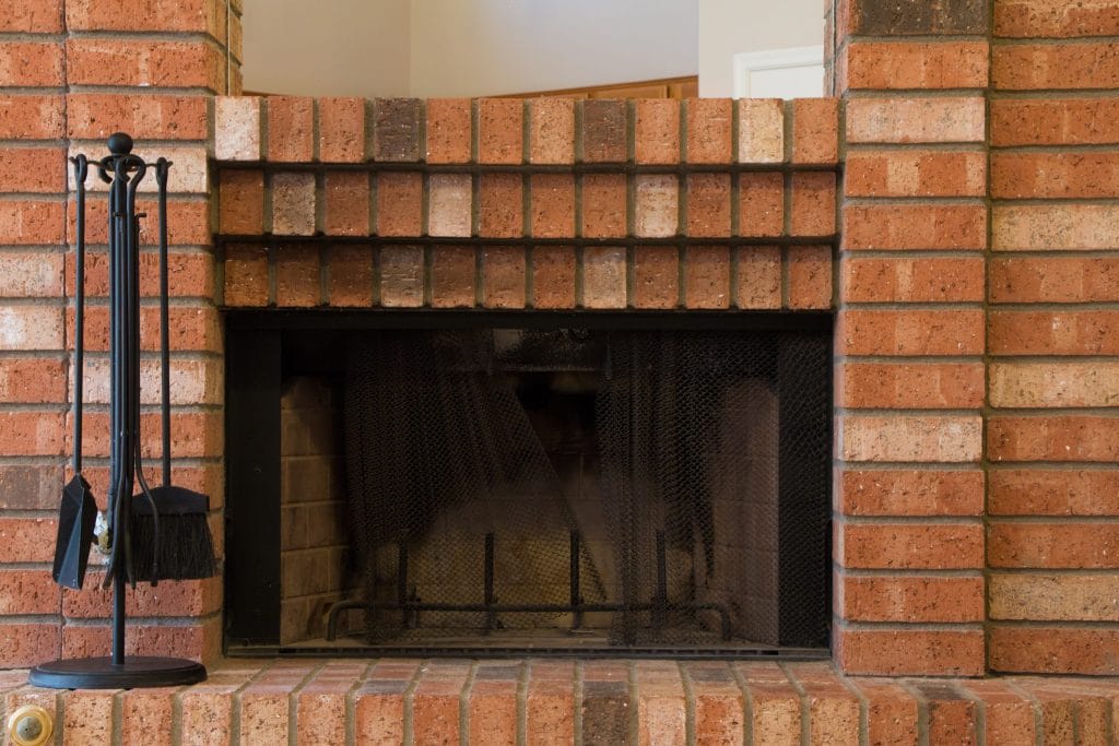 Empty brick masonry fireplace with a mesh screen and fireplace tools.